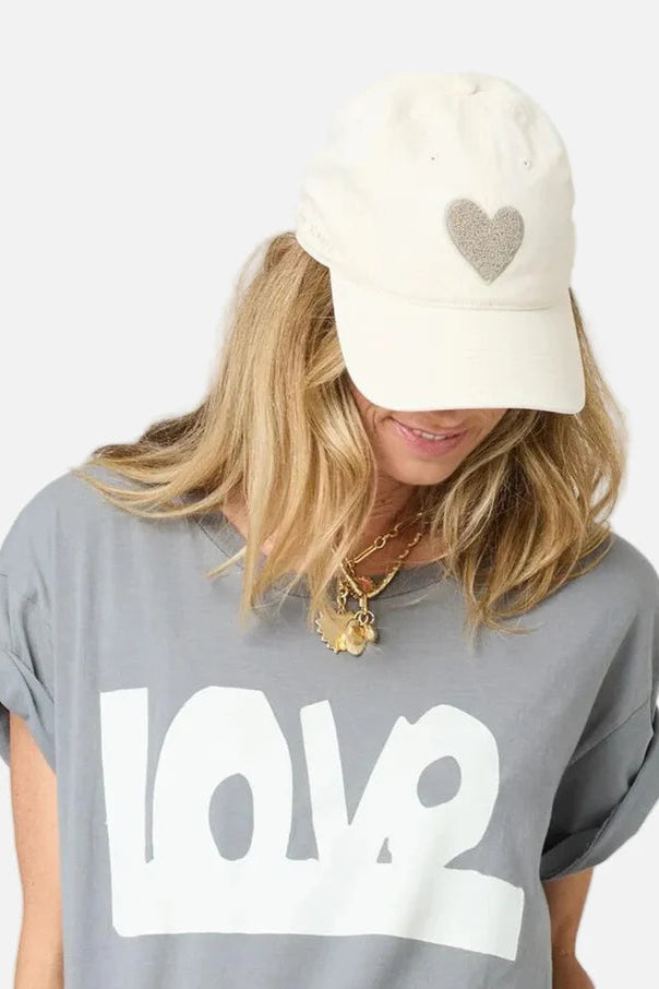 Woman wearing a cream baseball cap with a textured heart detail and “love always” embroidery on the side, front view