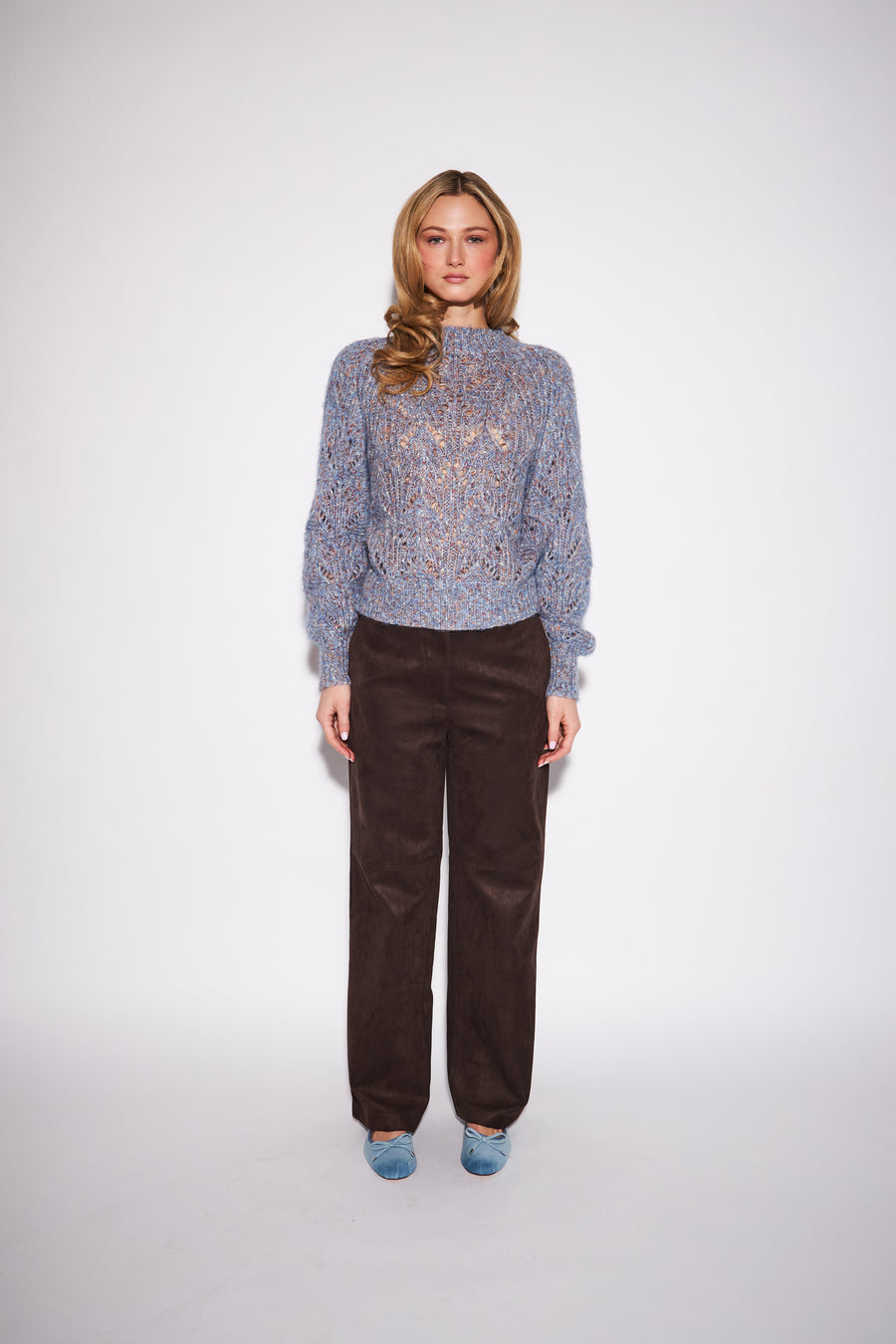 model wearing a blue marled knit mock neck sweater with round balloon sleeves against a neutral studio backround 