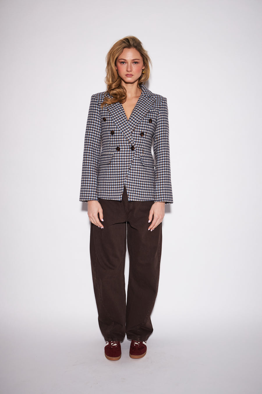 model wearing a black and white houndsooth double-breasted blazer with a neutral studio backround 
