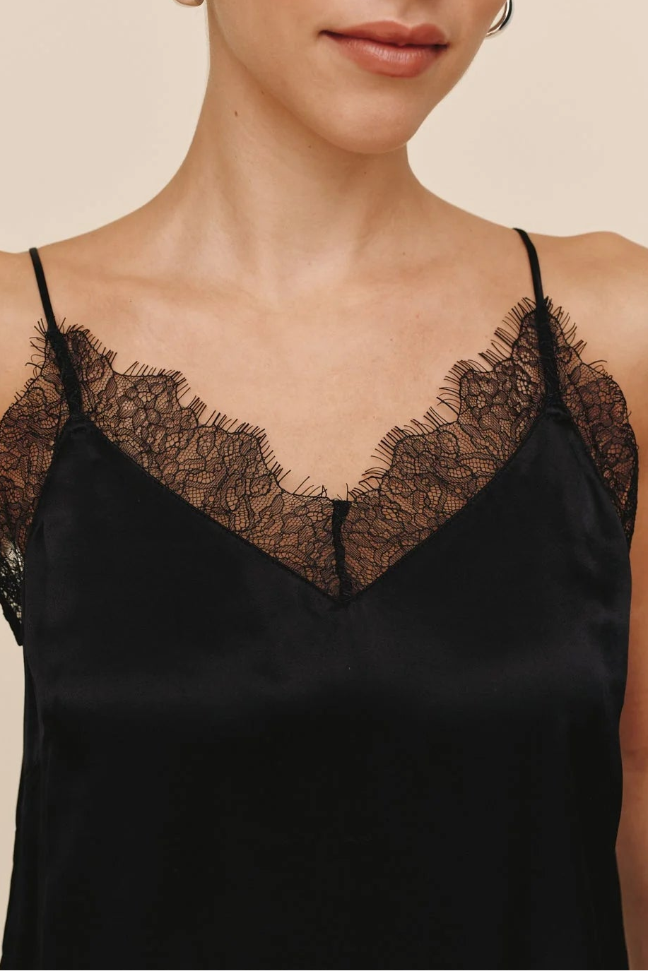 Woman wearing a black lace-trimmed top against a beige background