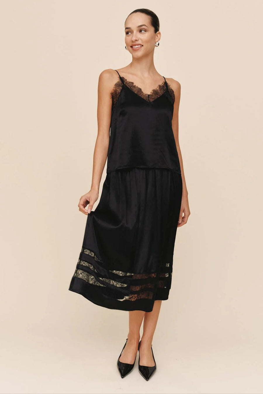 Woman wearing a black lace matching top and skirt against a beige background