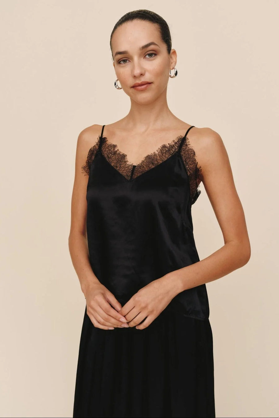Woman wearing a black satin slip top with lace trim against a beige background