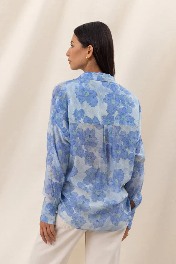 Woman wearing a blue floral long-sleeve button-up blouse with a relaxed fit, back