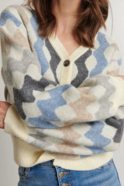 Person wearing a patterned sweater with blue, gray, and beige colors on a plain background