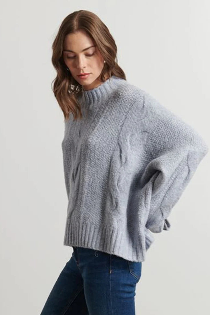 Woman wearing a light blue cable knit sweater and blue jeans on a light background