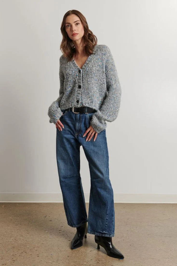Woman wearing a gray cardigan and blue jeans standing against a plain background