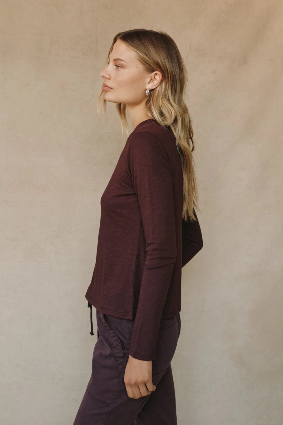 Side view of woman wearing a burgundy long sleeve crew neck tee
