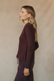 Side view of woman wearing a burgundy long sleeve crew neck tee