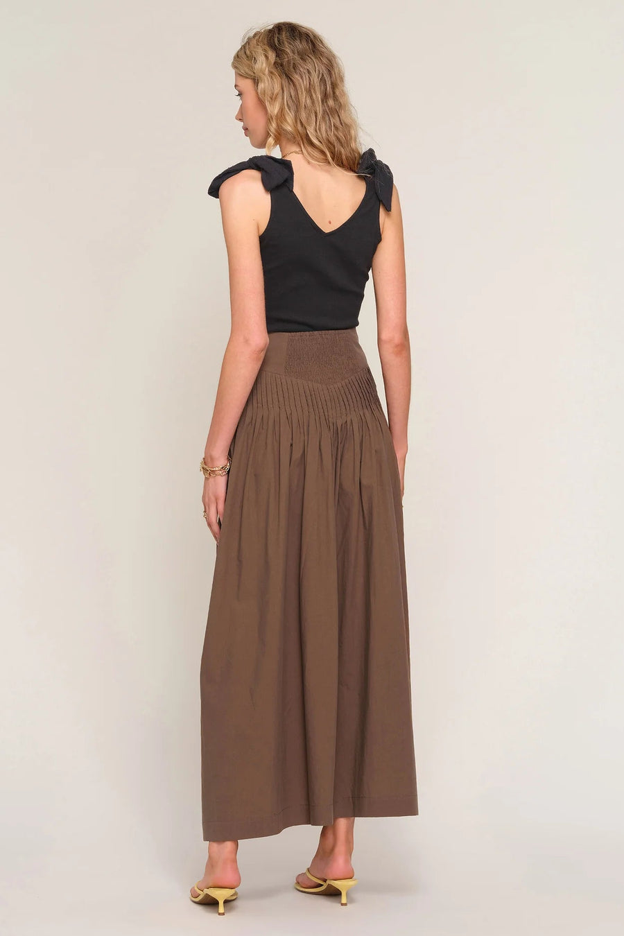 woman wearing a brown high-waisted pleated maxi skirt, back