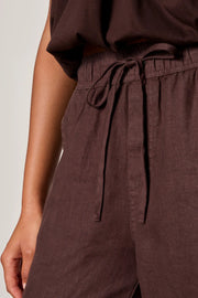 Woman wearing rich chocolate brown jogger-style pants with a relaxed fit. Features an elastic drawstring waistband, side pockets, and elasticized ankle cuffs. Crafted from a lightweight woven fabric with an easy, comfortable silhouette, closeup