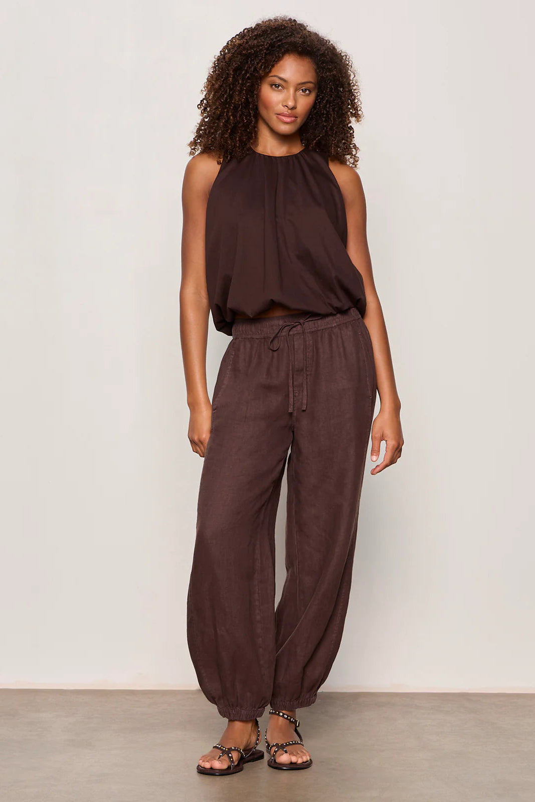 Woman wearing rich chocolate brown jogger-style pants with a relaxed fit. Features an elastic drawstring waistband, side pockets, and elasticized ankle cuffs. Crafted from a lightweight woven fabric with an easy, comfortable silhouette, front