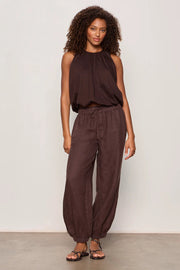 Woman wearing rich chocolate brown jogger-style pants with a relaxed fit. Features an elastic drawstring waistband, side pockets, and elasticized ankle cuffs. Crafted from a lightweight woven fabric with an easy, comfortable silhouette, front