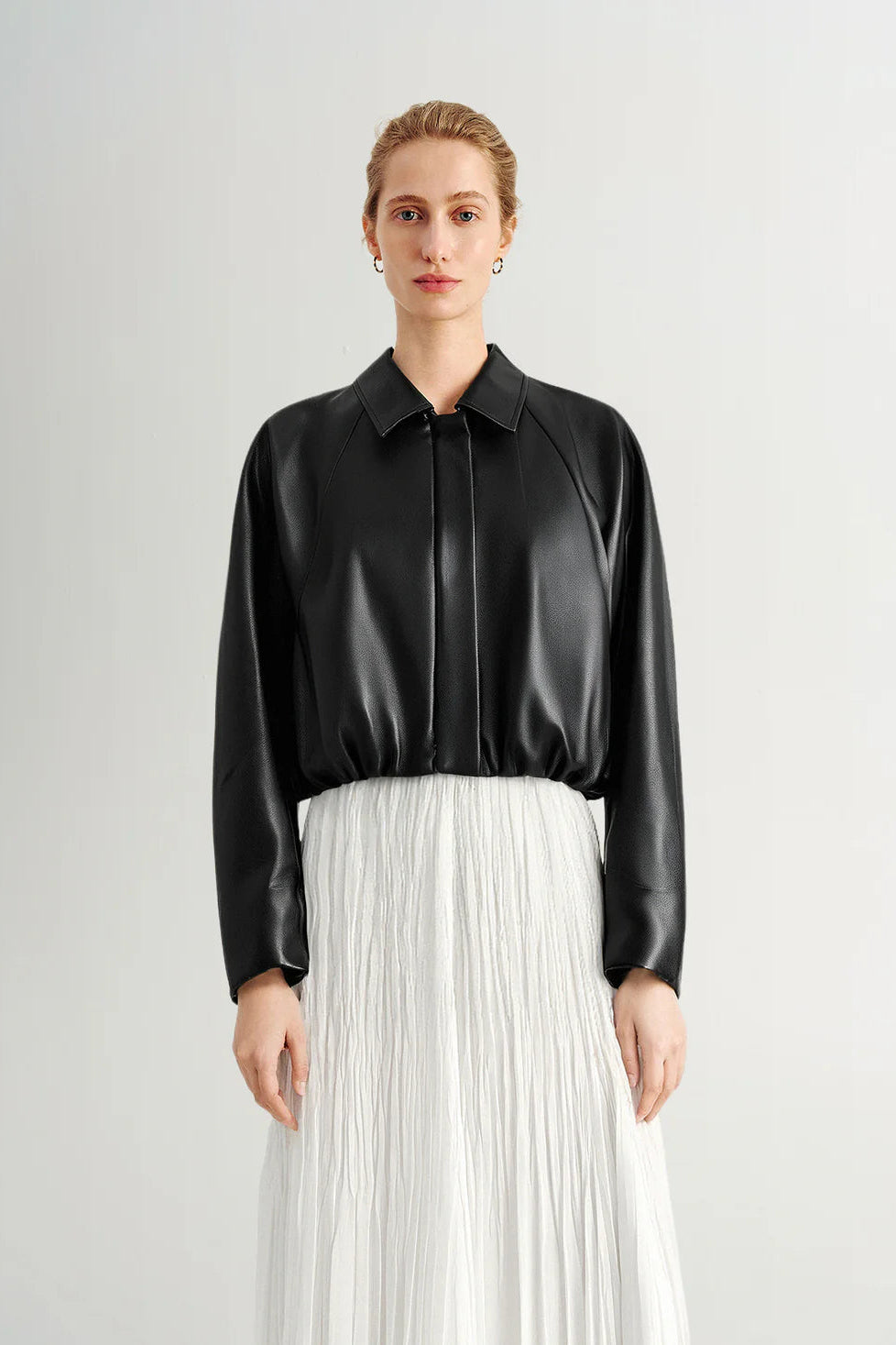 Woman wearing a black long-sleeve collared faux leather jacket, front