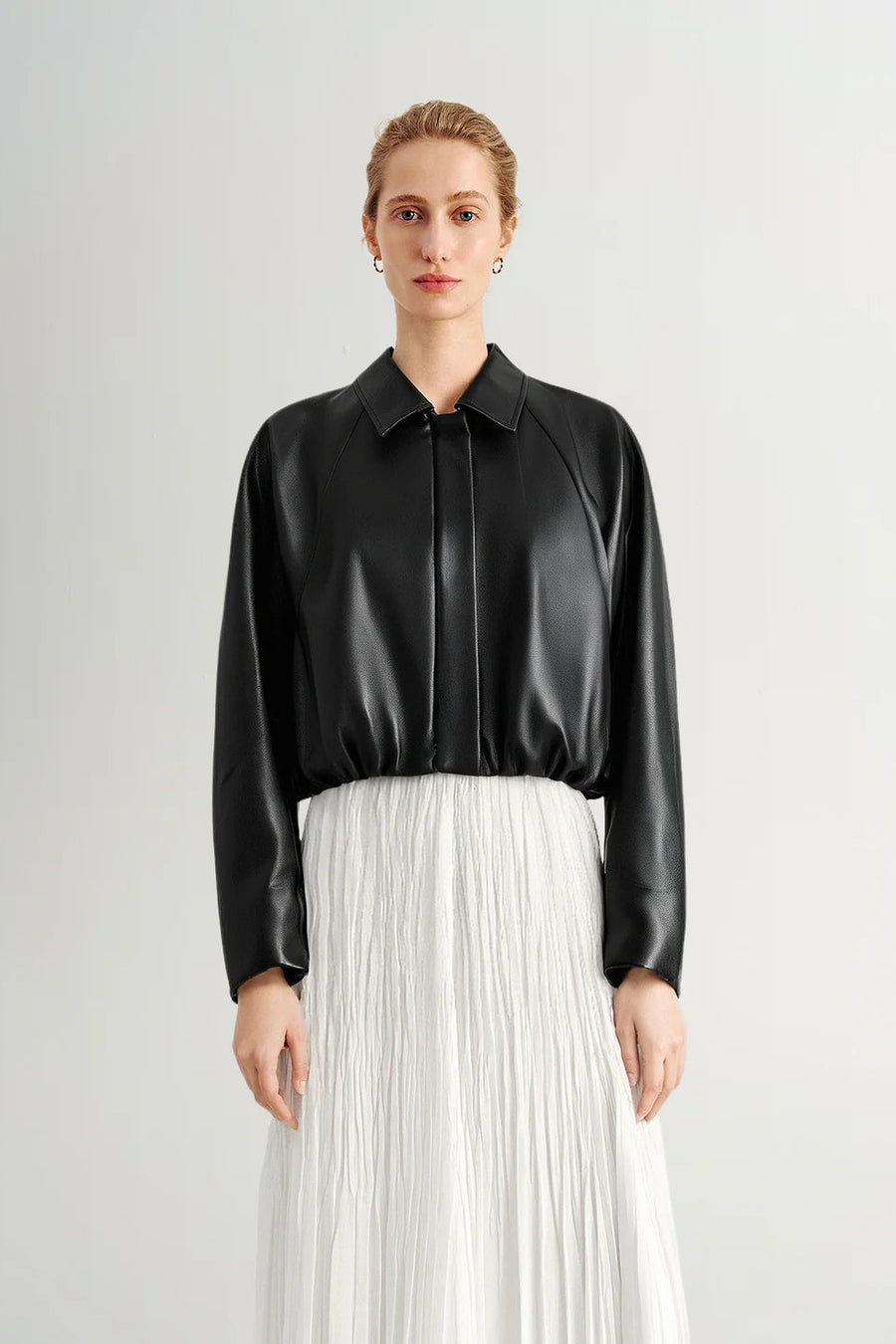 Woman wearing a black long-sleeve collared faux leather jacket, front