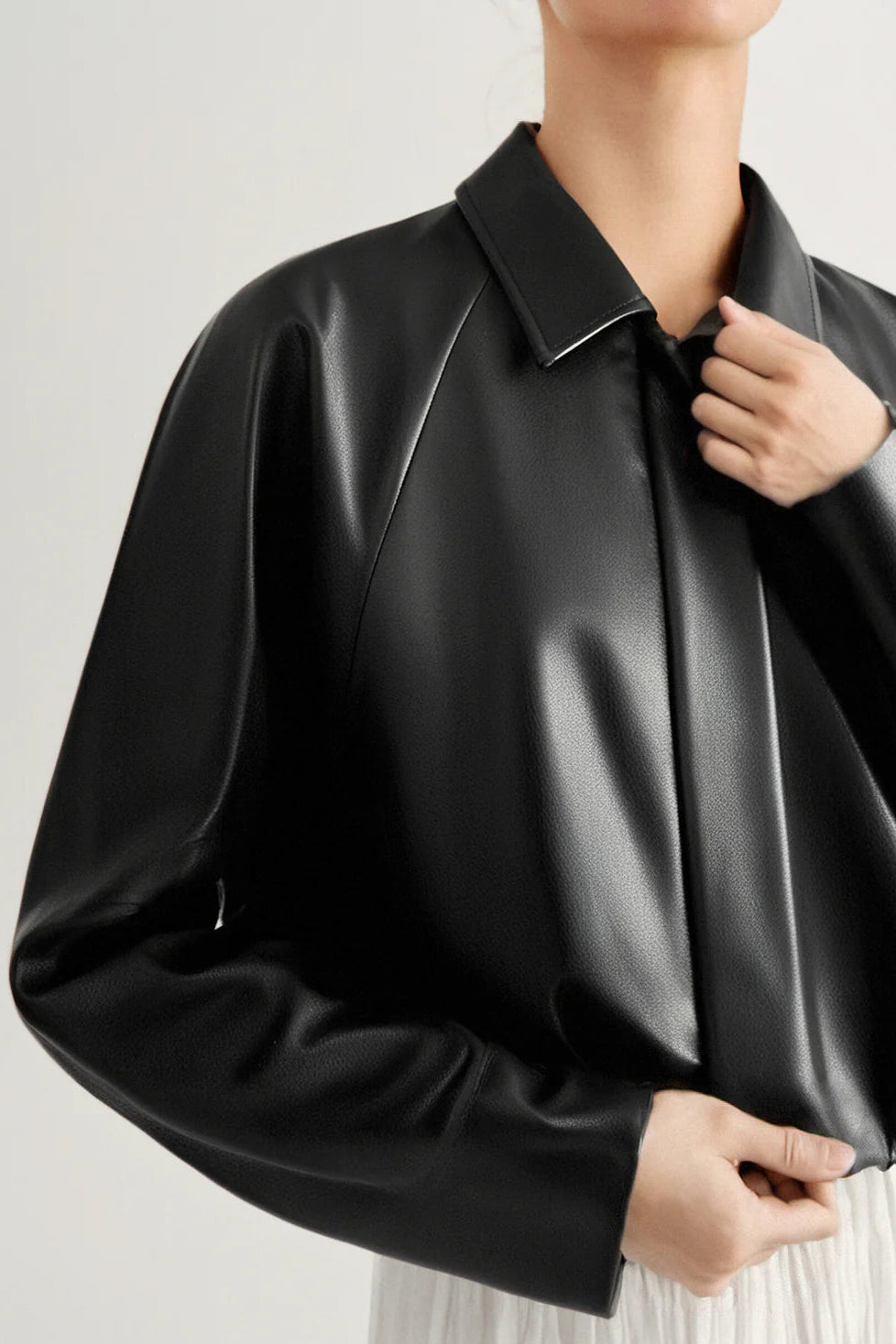 Woman wearing a black long-sleeve collared faux leather jacket, side detail