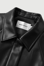 Woman wearing a black long-sleeve collared faux leather jacket, colar detai