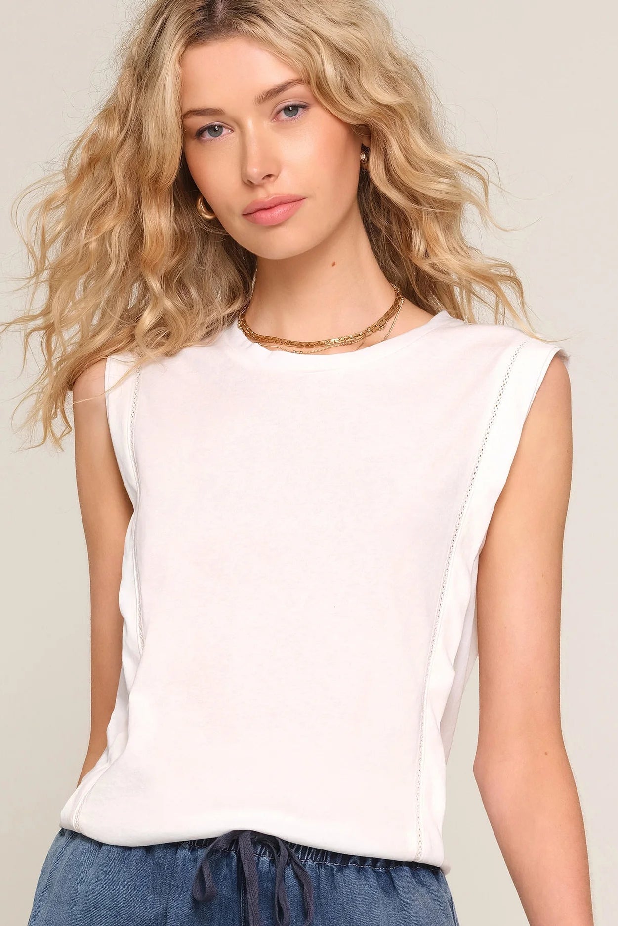 woman wearing a white sleeveless top with a relaxed fit paired with blue drawstring shorts, front
