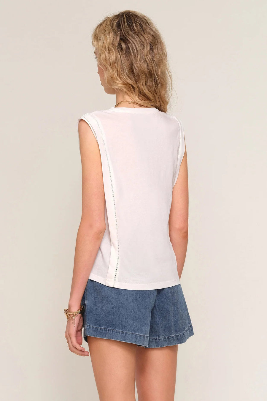 woman wearing a white sleeveless top with a relaxed fit paired with blue drawstring shorts, back