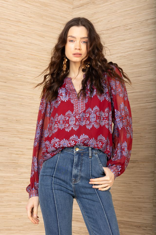 Front view of woman wearing a red background and blue patterned long sleeve blouse tucked into jeans