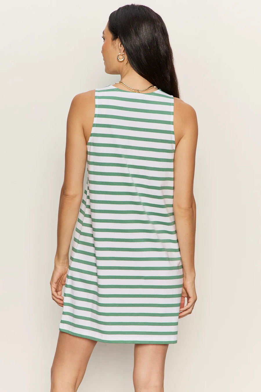 Woman wearing a sleeveless white shift dress with soft sage green horizontal stripes. The dress features a high crew neckline, an easy A-line silhouette, and falls above the knee, back