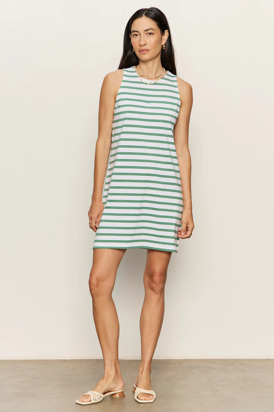 Woman wearing a sleeveless white shift dress with soft sage green horizontal stripes. The dress features a high crew neckline, an easy A-line silhouette, and falls above the knee, front