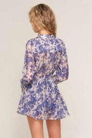 woman wearing a blue floral long-sleeve mini romper with a button-front neckline, cinched waist, and flowy skirt, back