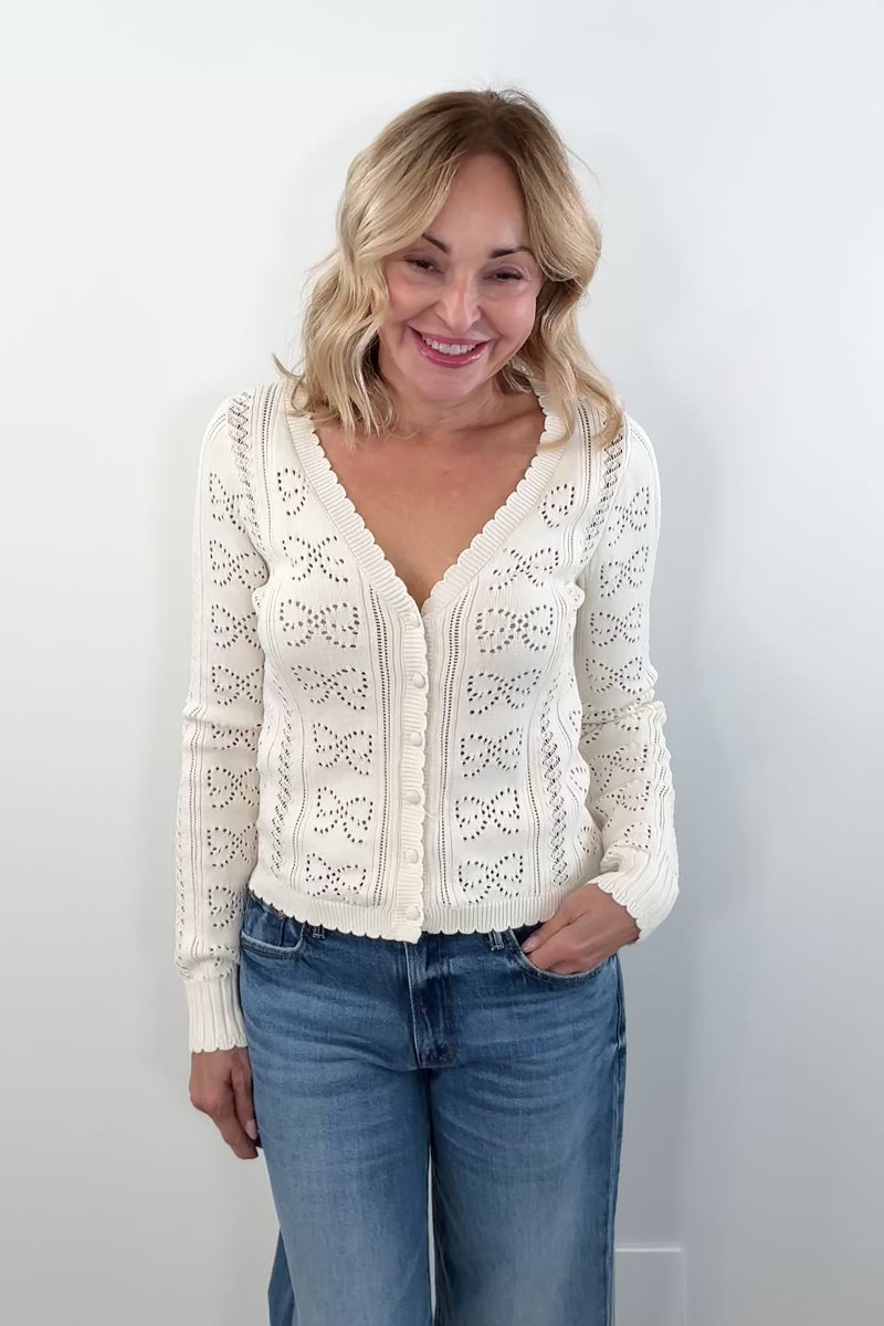 video of woman wearing a cream cardigan with buttons on the front scalloped trim and openwork