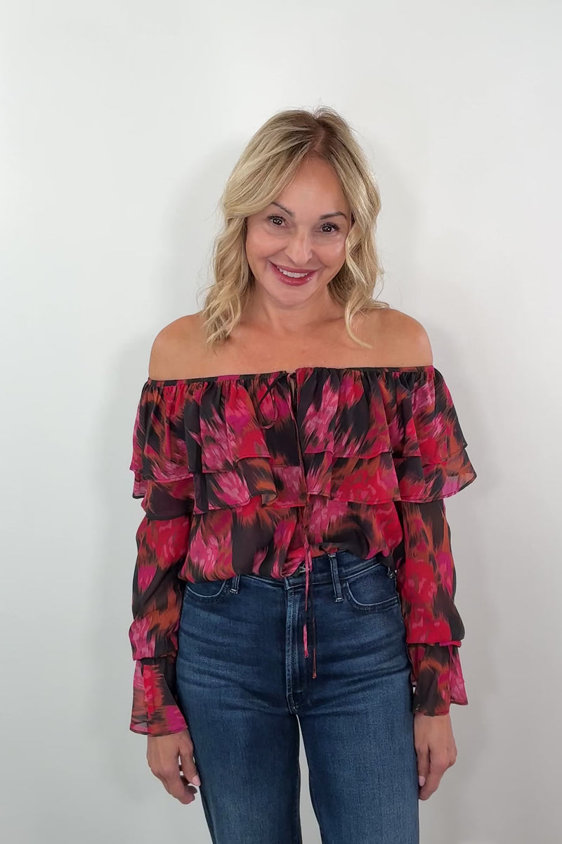 Video of a woman wearing a red and black floral boat-neck top with blue jeans