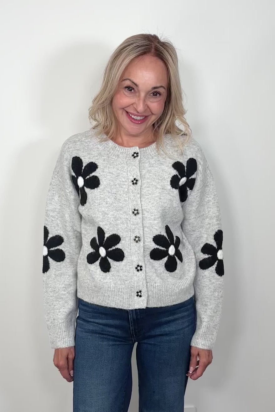 Video of woman wearing a gray cardigan with a black daisy pattern and buttons, done up and turning around to show the back