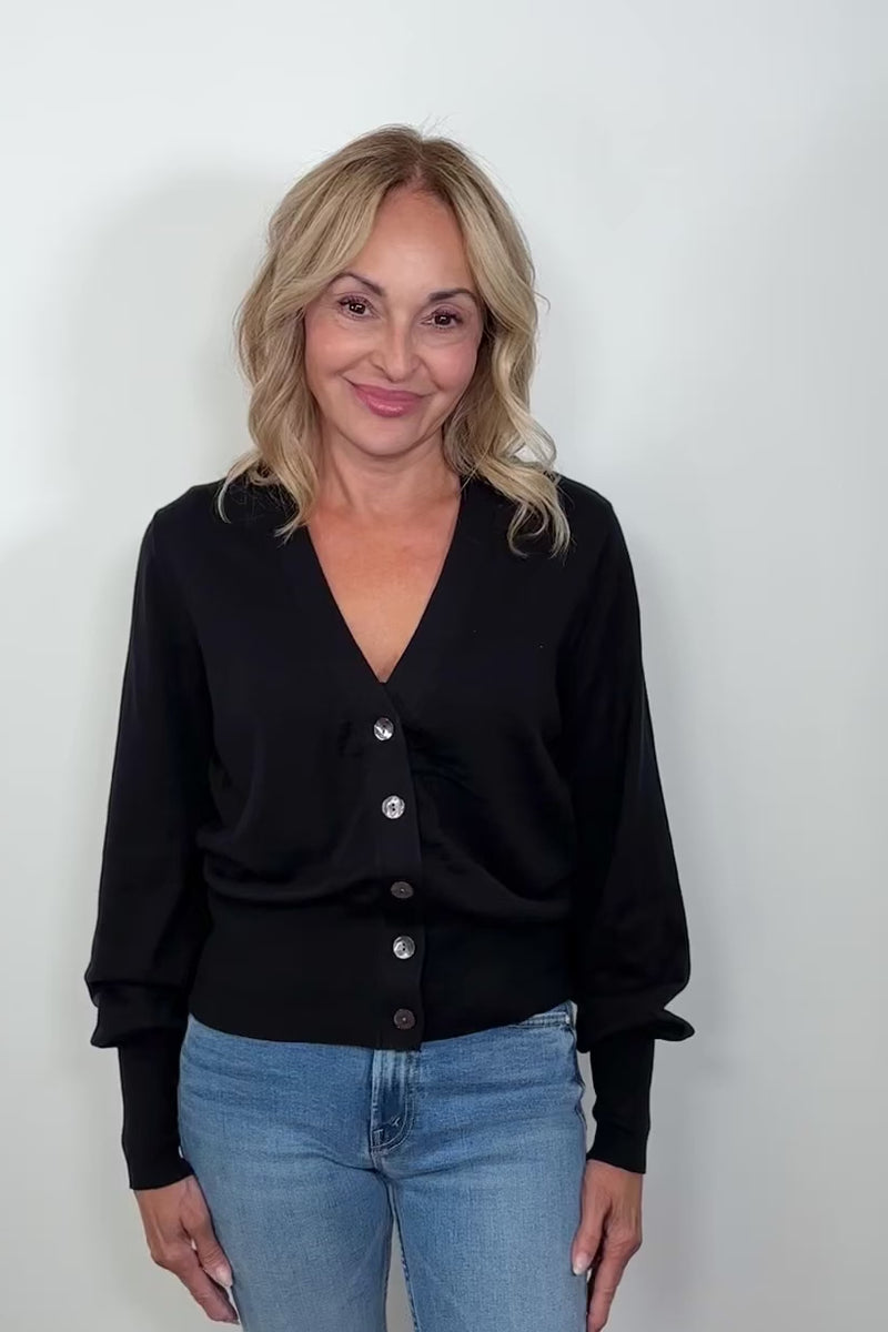 front facing woman wearing a black cotton, silk and cashmere blend cardigan with extended cuffs closed turning around to show the back.