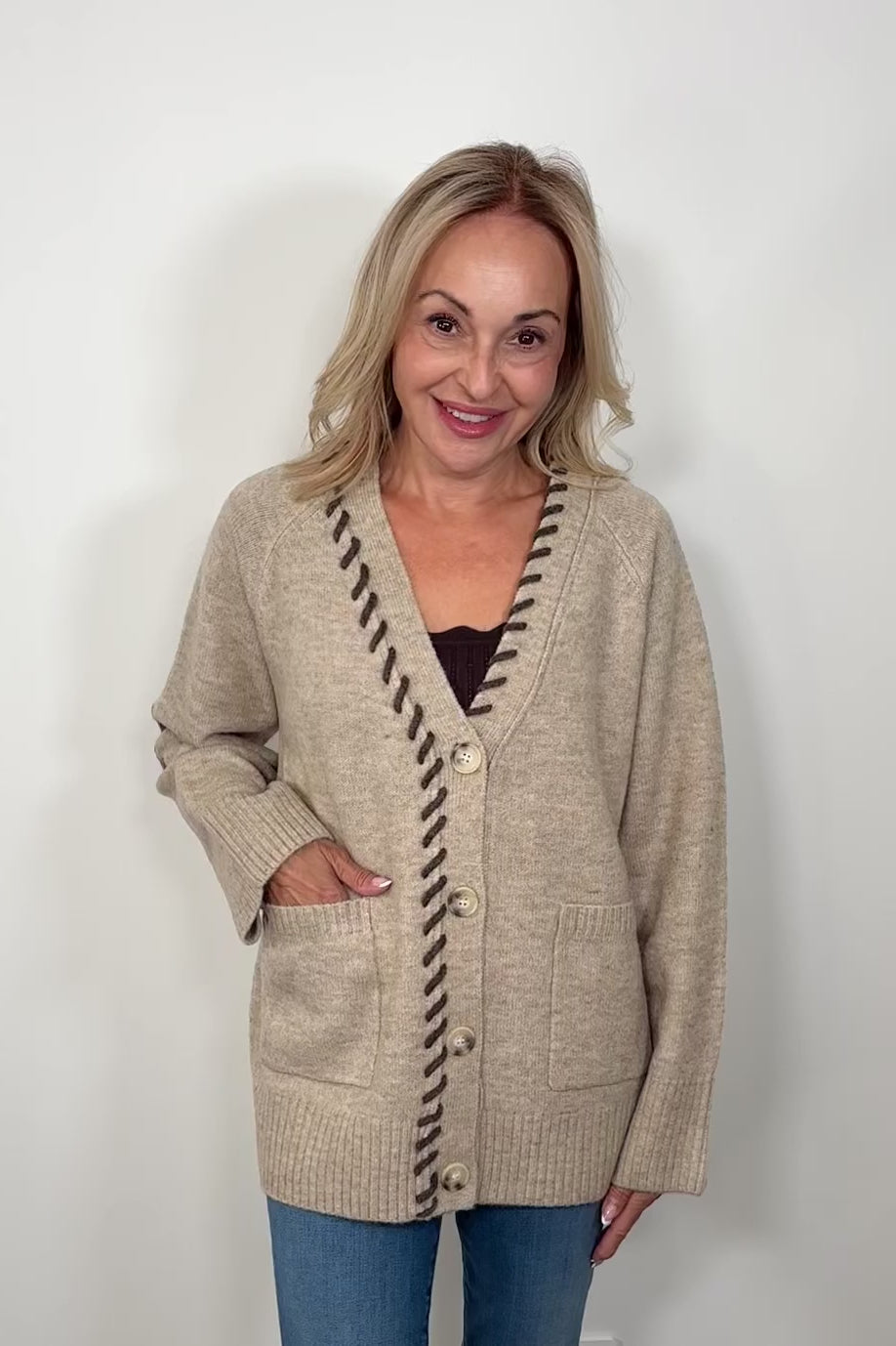 Video of woman wearing a beige cardigan, v-neck and brown detailing turning around to show the back