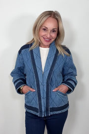 Front facing woman wearing a blue quilted jacket with navy blue detailing. She is turning to show the back of the jacket.