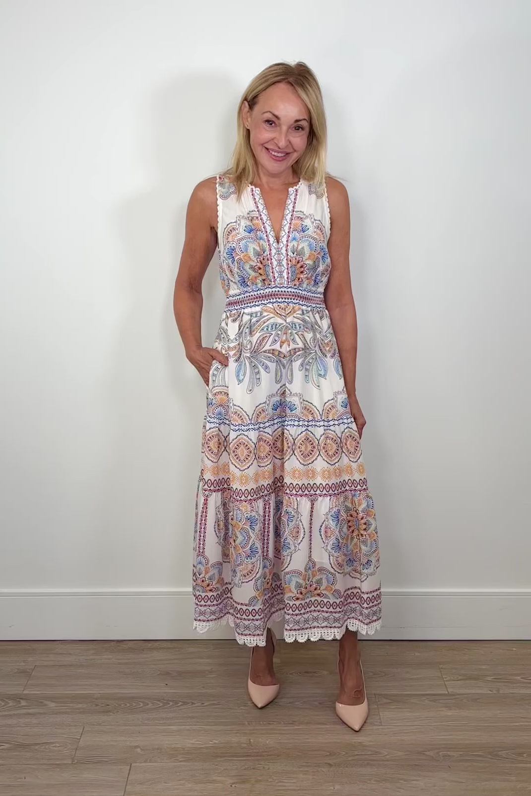 Video of a woman wearing white sleeveless midi dress with a blue, red and orange pattern as well as crochet detailing turning around to show the back