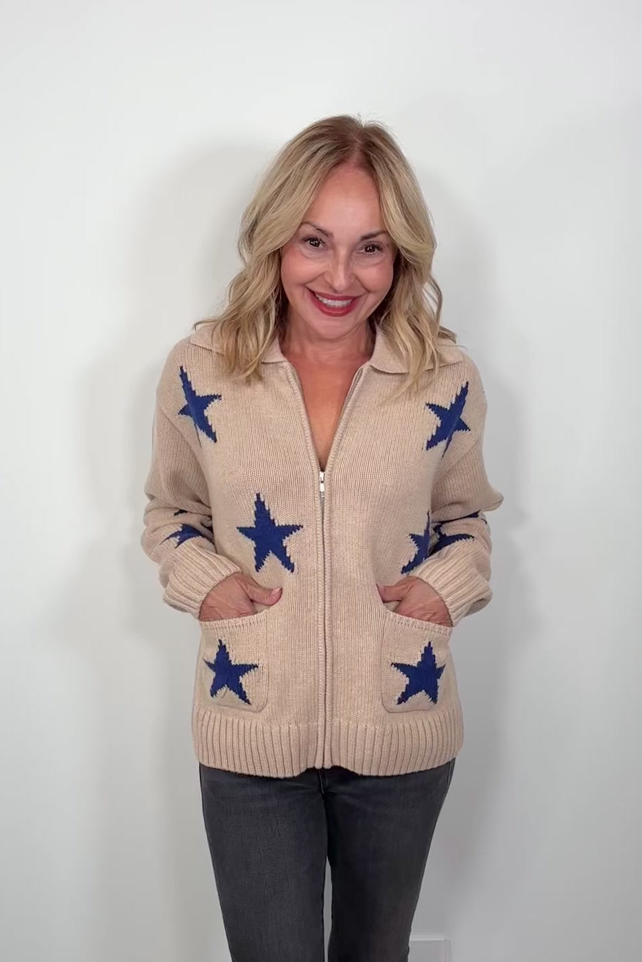 Video of a woman wearing a beige zip-up sweater with blue star patterns and front pockets