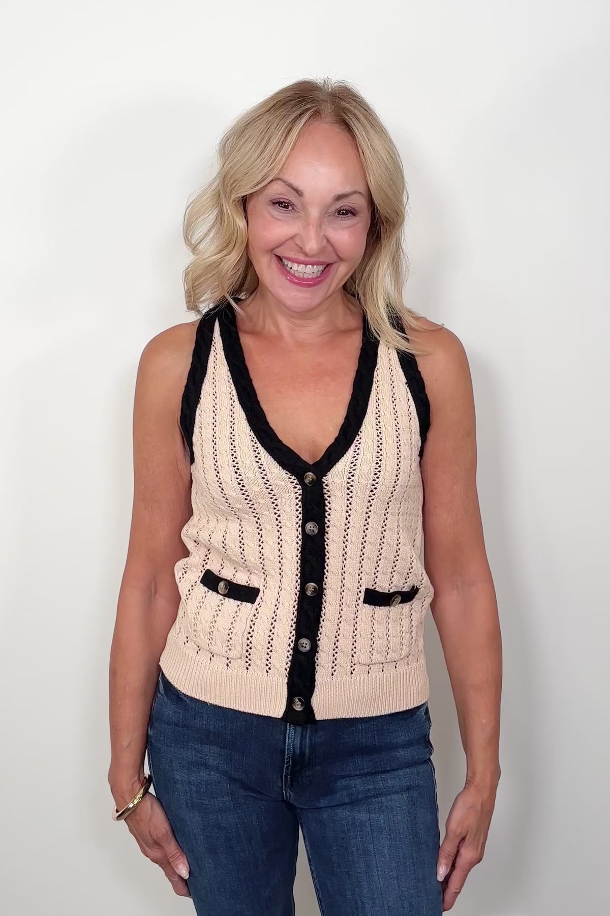 video of a woman wearing a beige knitted vest with black trim on a white background