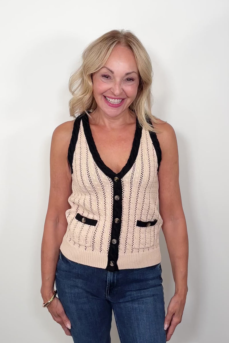 video of a woman wearing a beige knitted vest with black trim on a white background