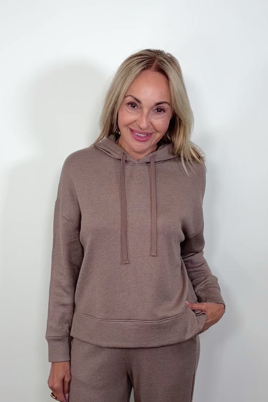 Video of  a woman wearing a matching set of light brown hoodie and pants on a white background
