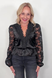 video of a woman wearing a black lace sleeves v-neck top and black pants against a white background