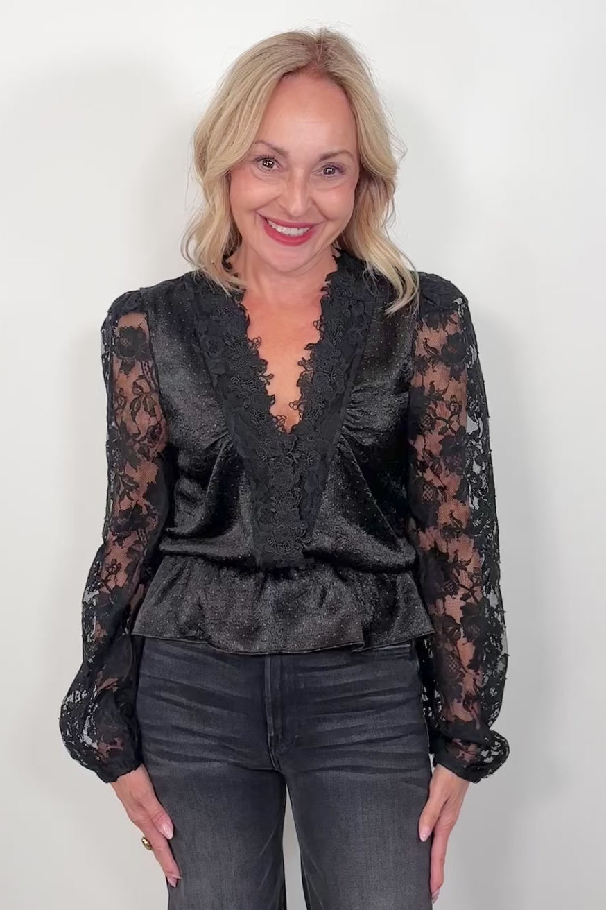 video of a woman wearing a black lace sleeves v-neck top and black pants against a white background