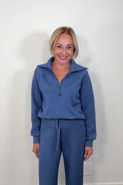Woman wearing a washed blue zip-up sweatshirt against a light gray background