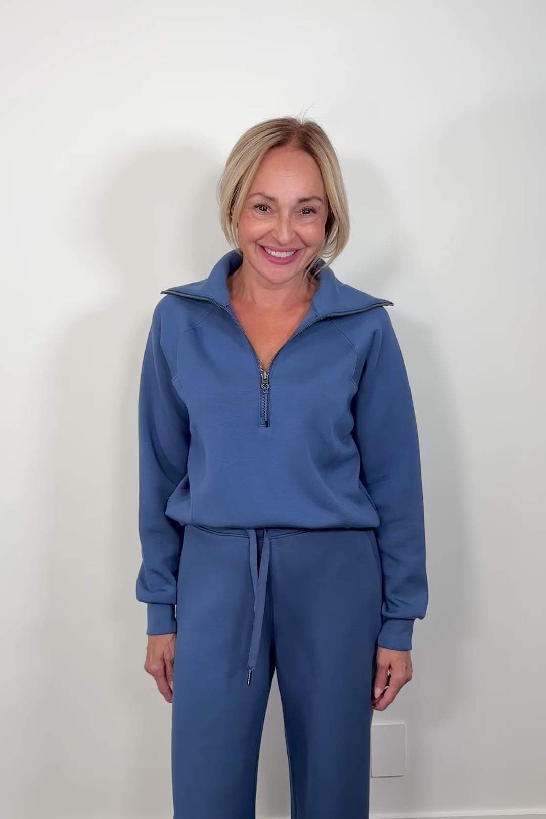 Woman wearing a washed blue zip-up sweatshirt against a light gray background