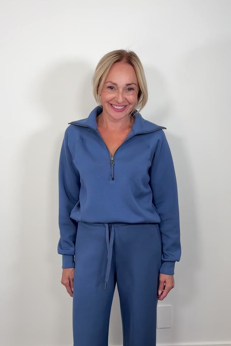 Woman wearing a washed blue zip-up sweatshirt against a light gray background