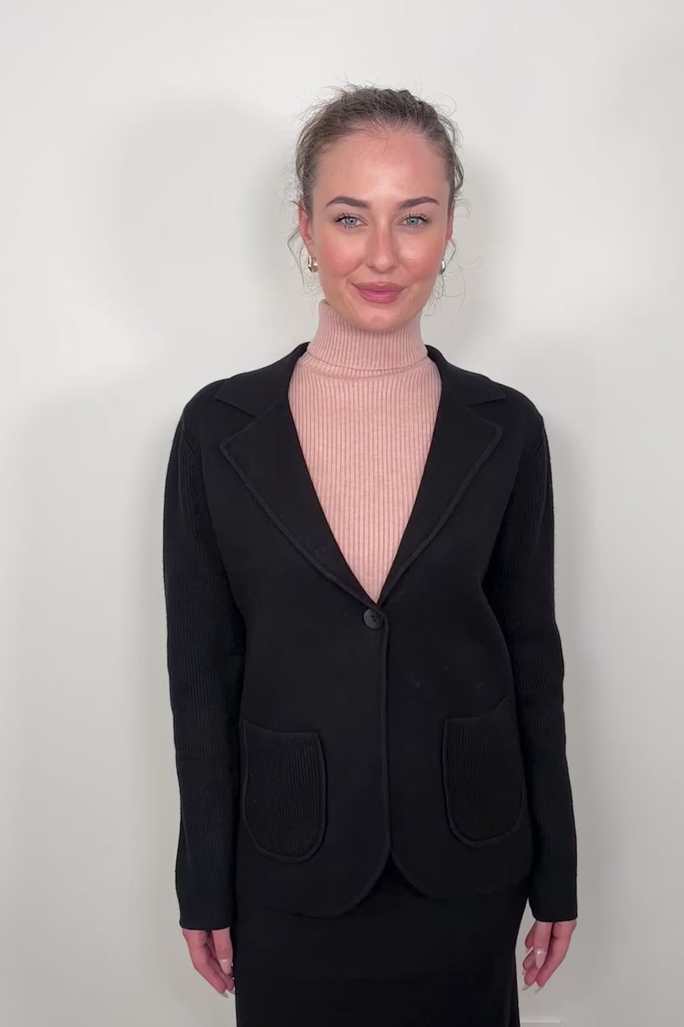 Video of woman wearing a black knitted jacket and a pink turtleneck tank top