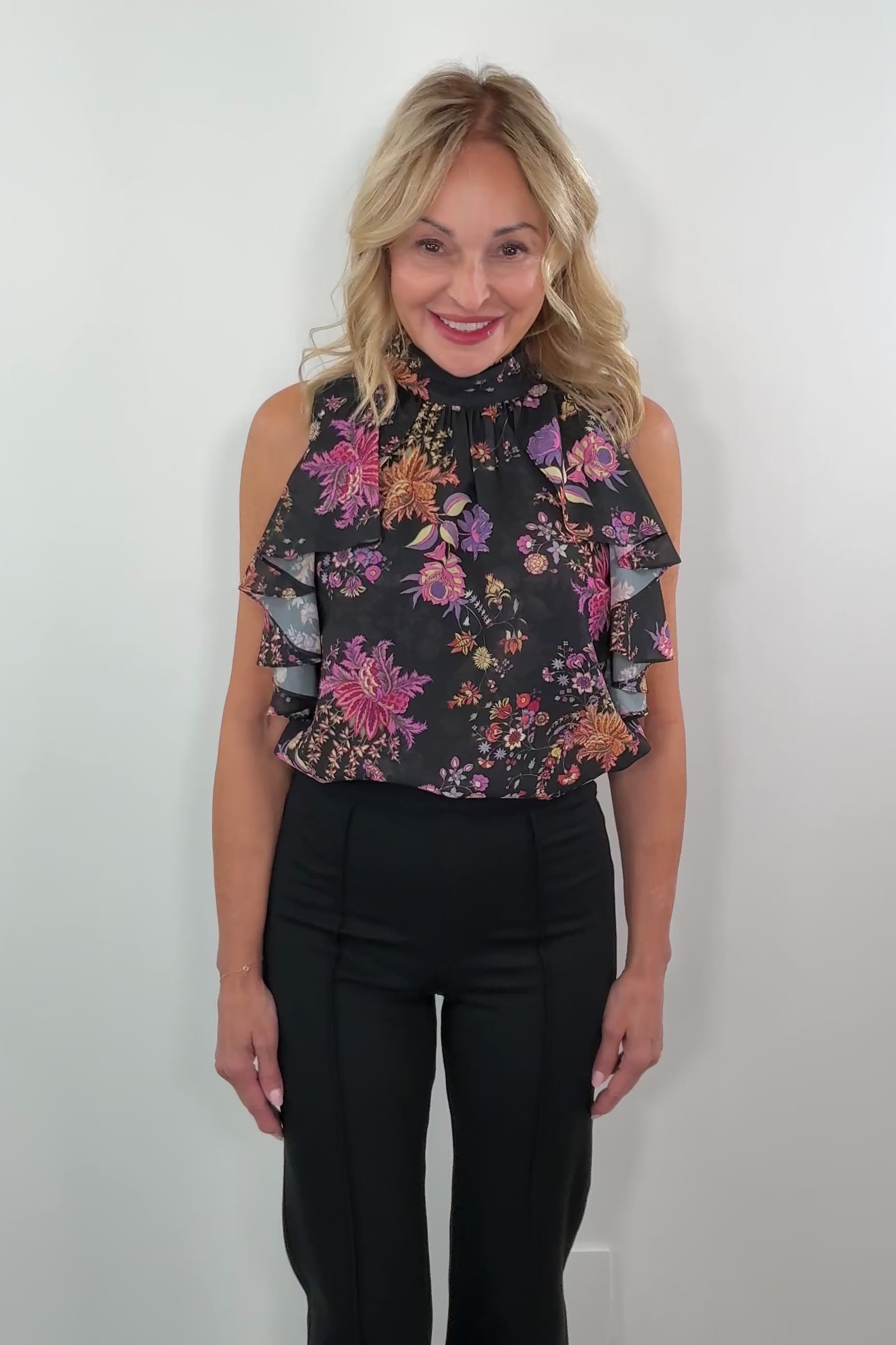 video of a woman wearing a black sleeveless flower patterned ruffle top