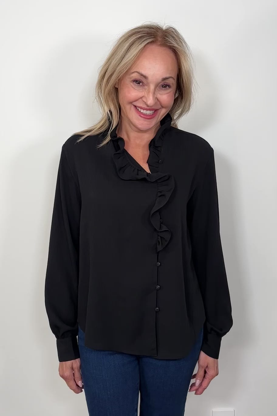 Video of a woman wearing a black blouse with ruffles and blue jeans 