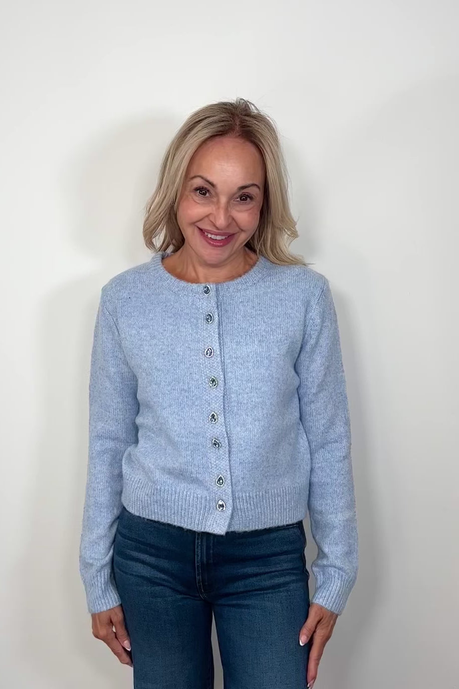Video of woman wearing a blue cardigan with gemstones as buttons done up turning around to show the garment.