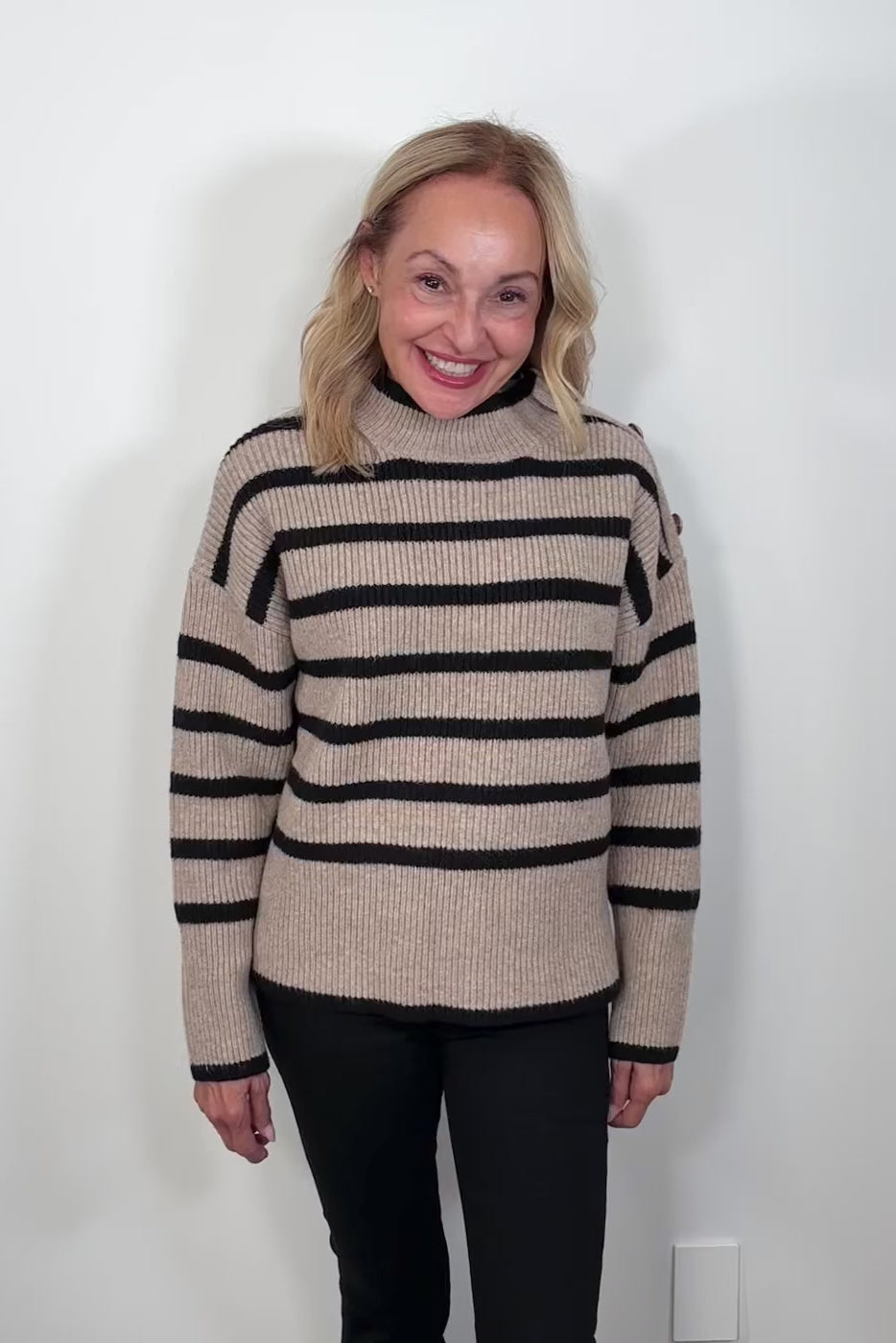 Video of a woman wearing a walnut coloured sweater with stripes and buttons on the left shoulder