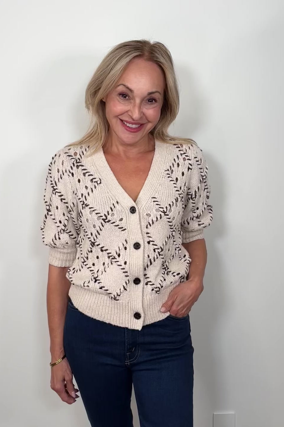 Video of a woman wearing a white knit cardigan with whipstitch detailing 