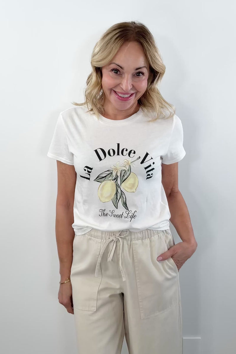 woman wearing white short sleeve graphic "la dolce vita" tee with pictures of lemon on the front