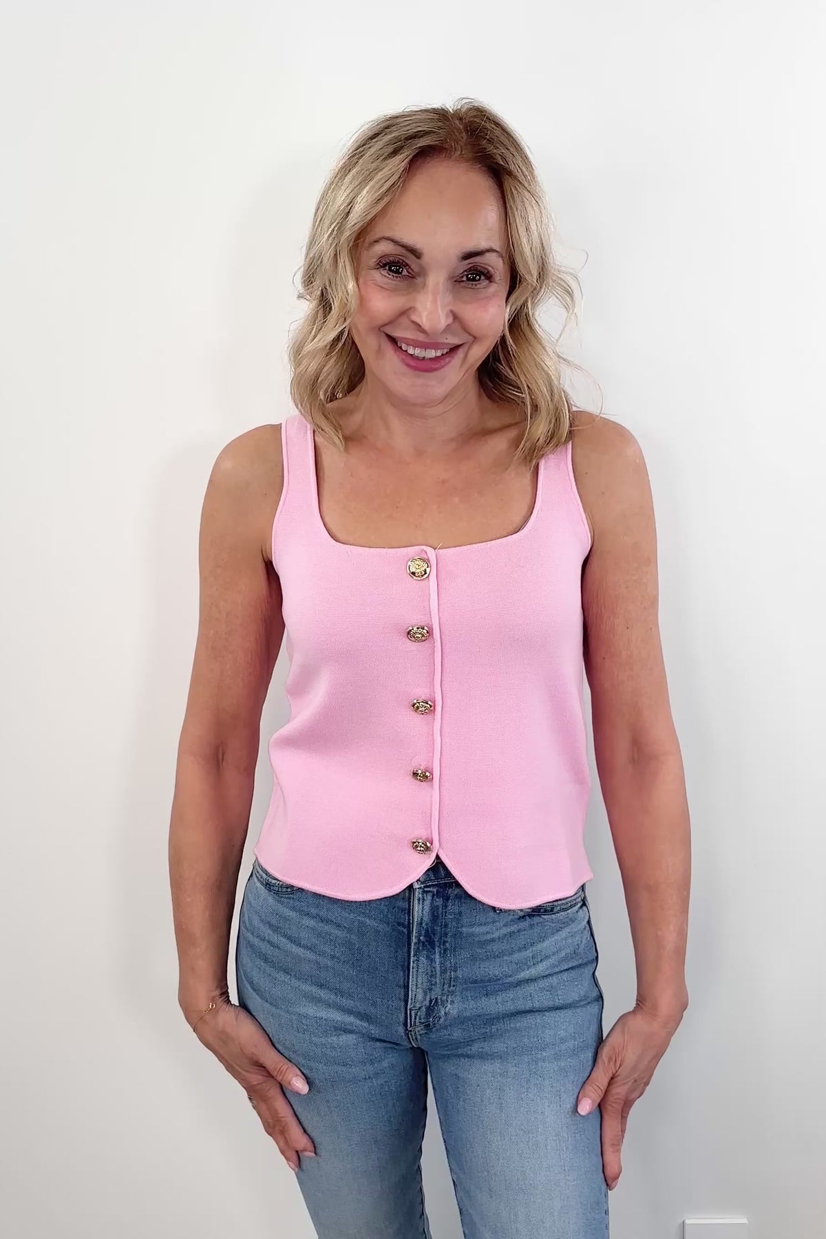 Video of a woman wearing a pink sleeveless knit tank top with front buttons and a scalloped hem